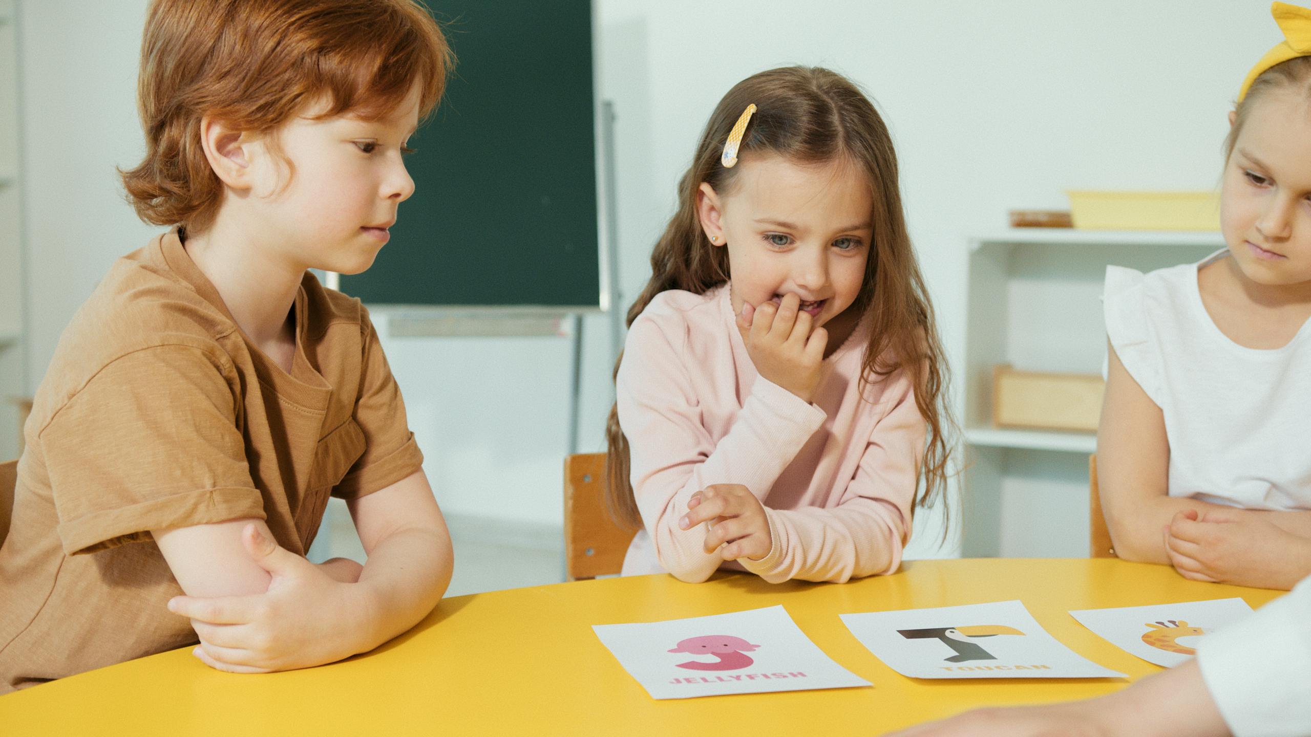 Group of kids engaging in a classroom activity with educational cards on a yellow table.